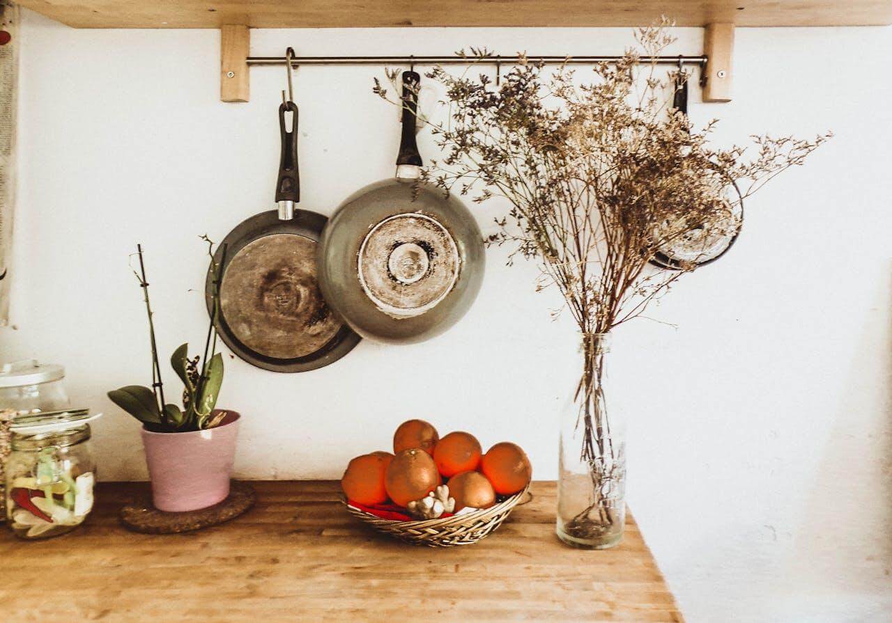 Rustic kitchen countertop with hanging pans, dried flowers, oranges in basket, and potted plant for home decor