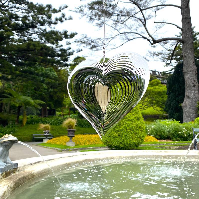 Heart-shaped wind spinner hanging near garden fountain, perfect for home decor and outdoor spaces