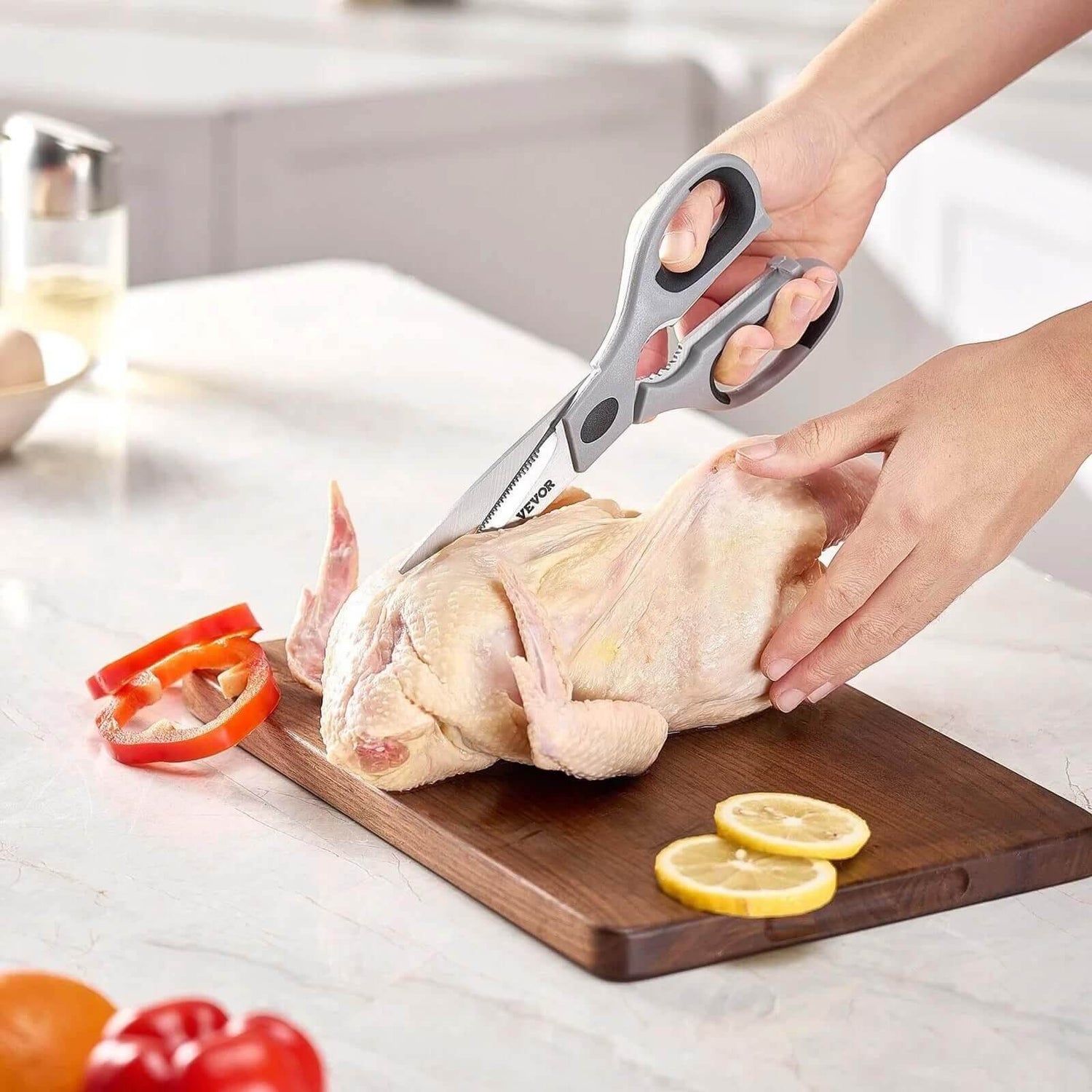 Heavy-duty kitchen shears cutting raw chicken on wooden board with lemon slices