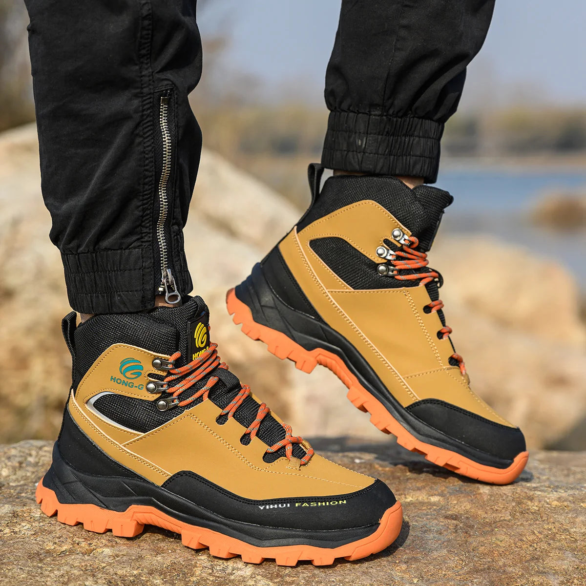 Tan and black hiking boots with orange soles worn by a person outdoors.